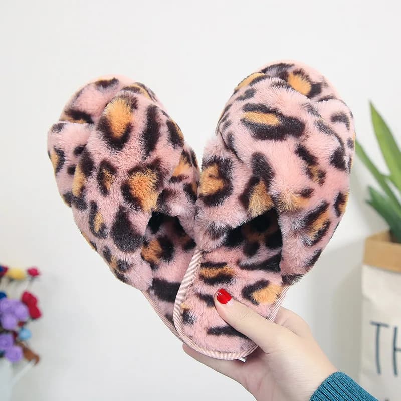 A hand holding up a pair of pink leopard print cross-strap fuzzy slippers