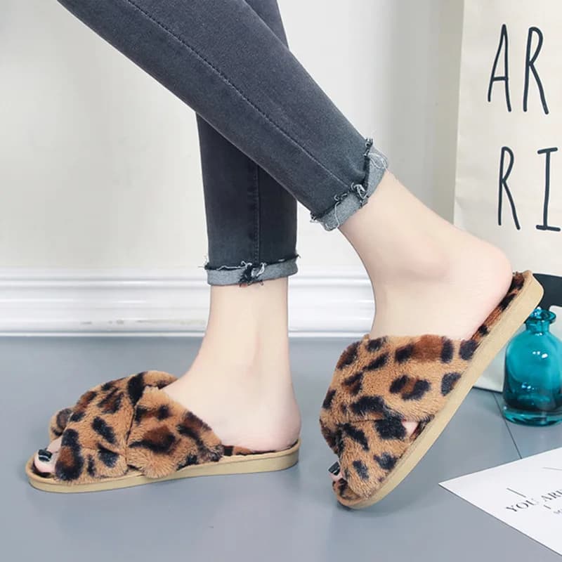 A person wearing fuzzy leopard print cross-strap slippers with dark grey jeans