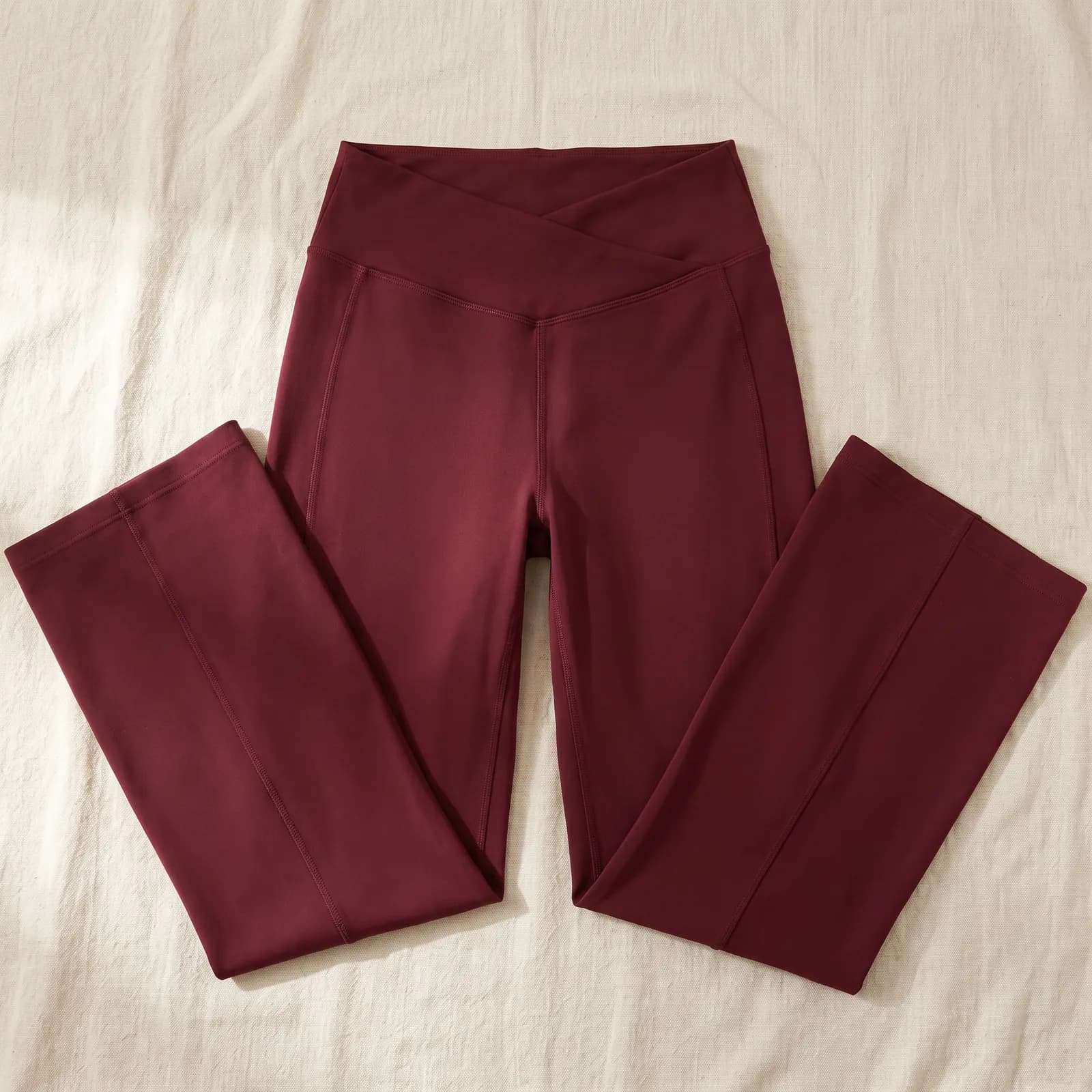 The pants laid flat top-down on warm cream linen, V waistband visible