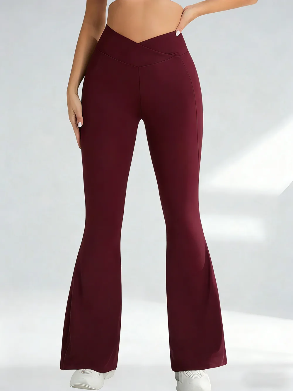 A person wearing burgundy crossover flare yoga pants against a plain background