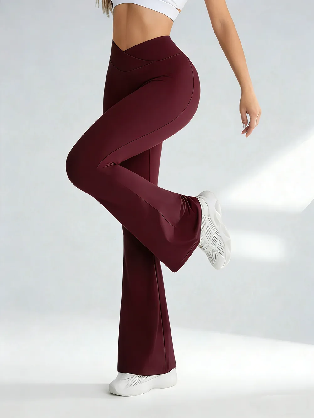 A woman wearing burgundy crossover flare yoga pants against a plain background