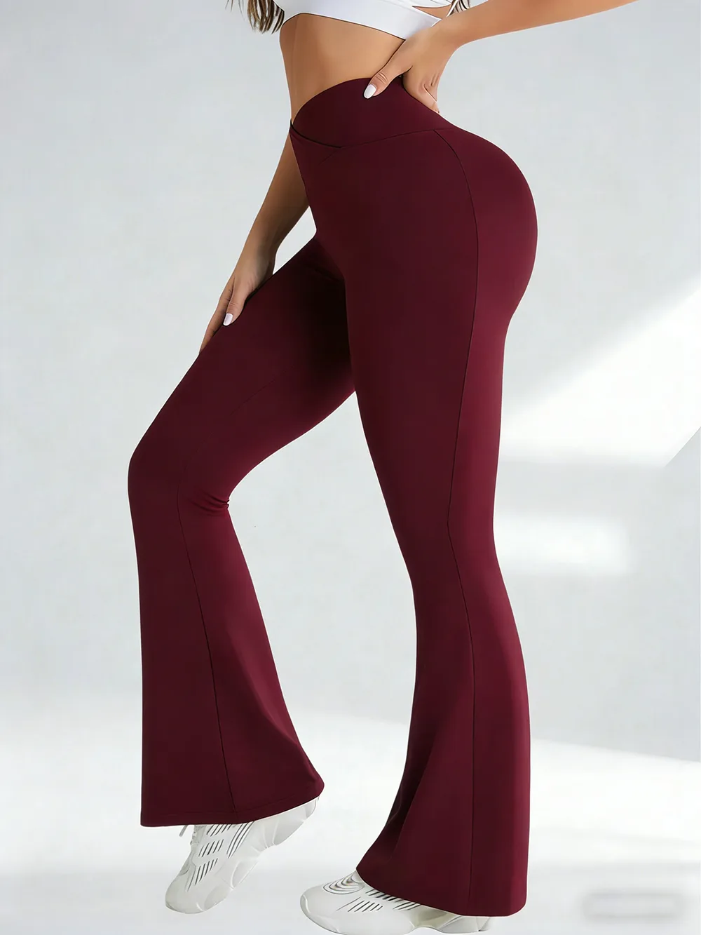A side view of a woman wearing burgundy crossover flare yoga pants against a plain background