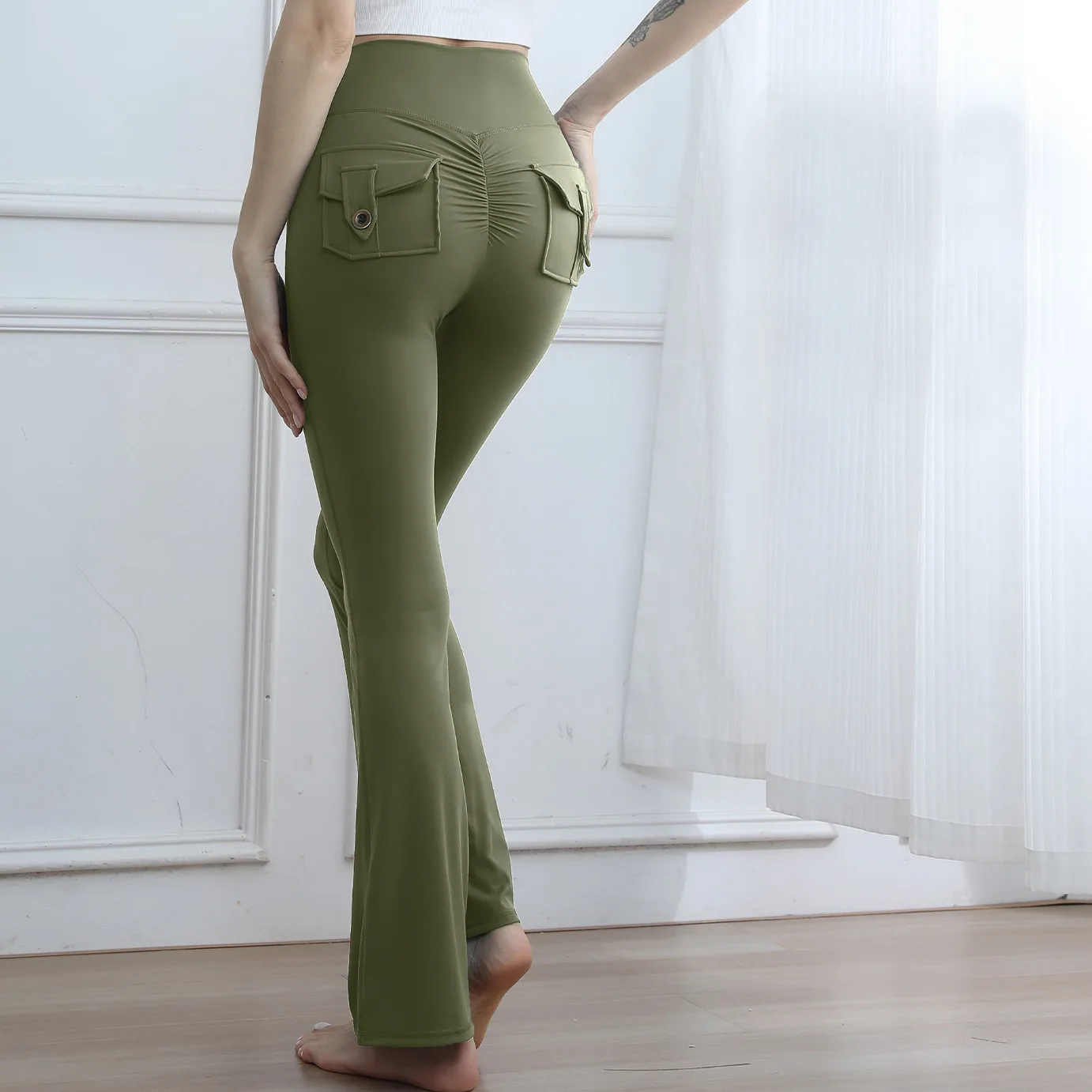 A woman wearing olive green flare leggings with back pockets and a ruched detail, viewed from behind