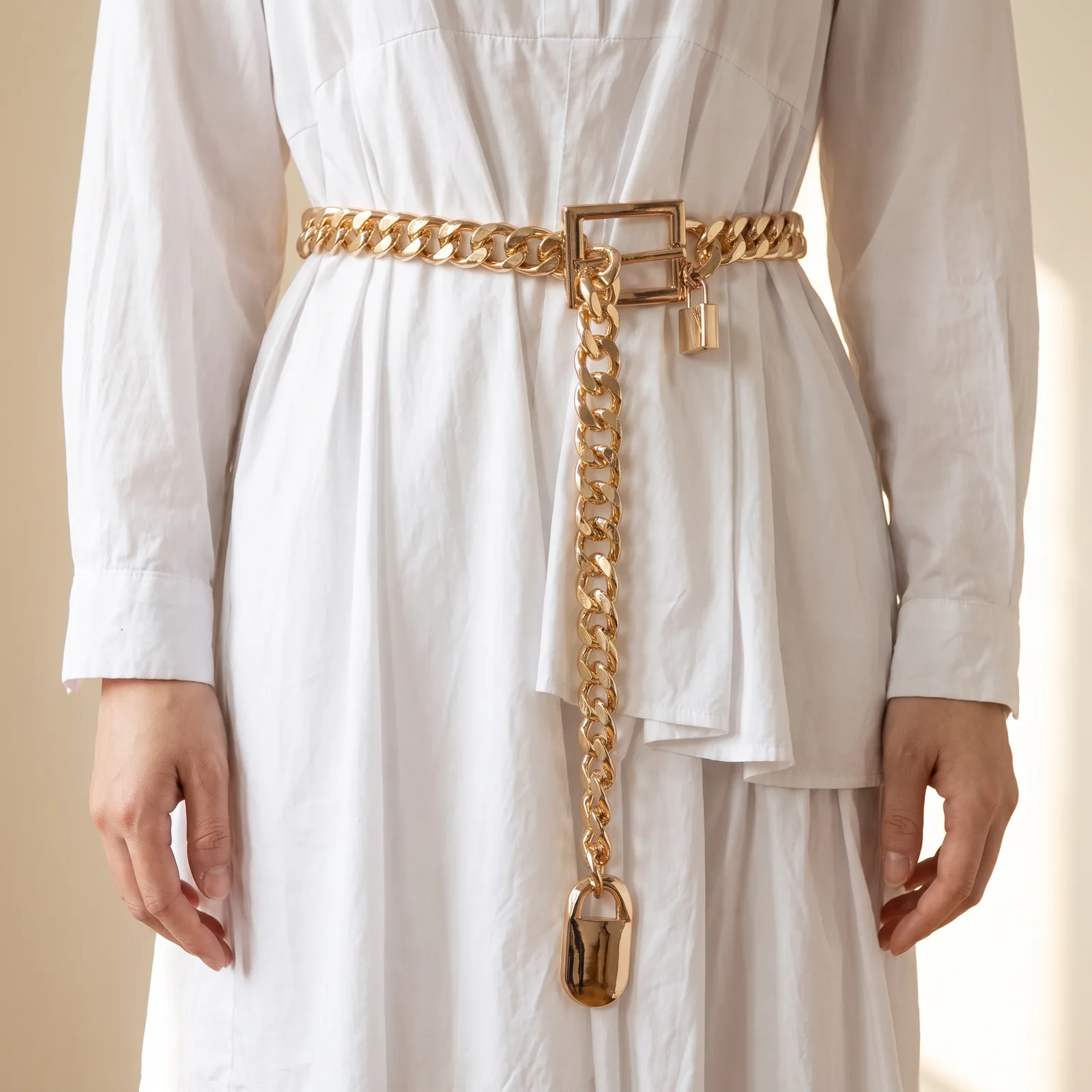A chain belt worn over a white dress at the waist, from the shoulders down, no face