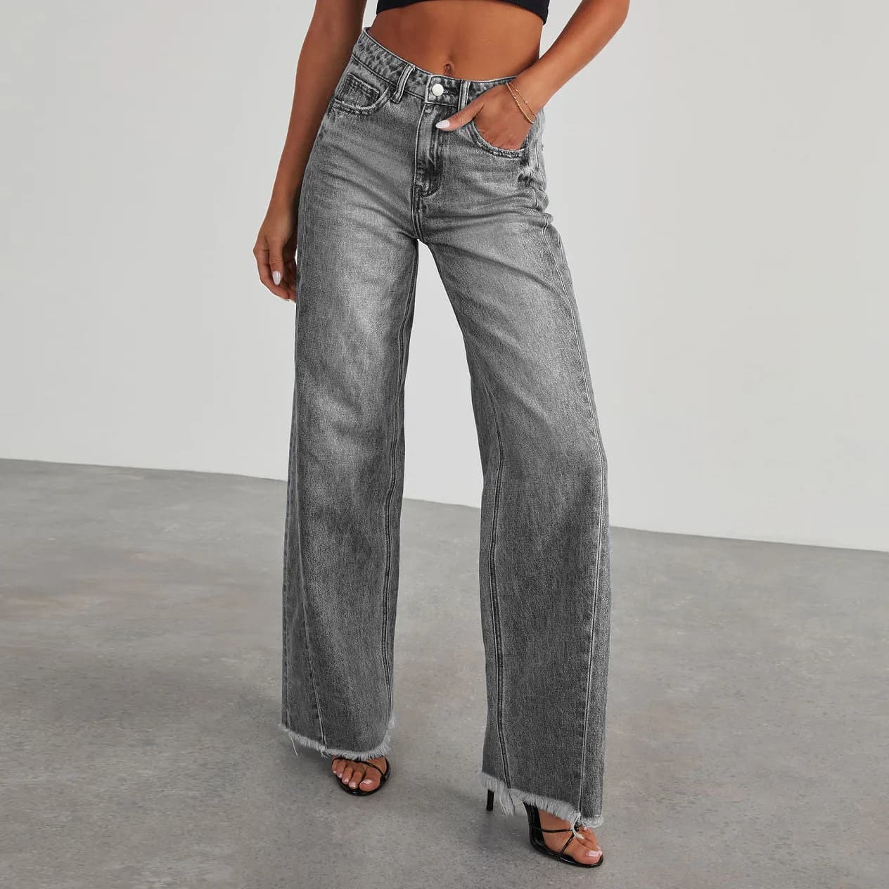 A woman wearing high-waist wide-leg grey jeans with a raw hem against a plain background