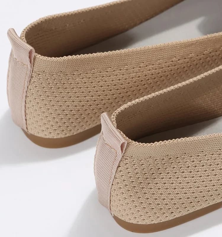A close-up view of the heel detail of beige knit ballet flats on a white background