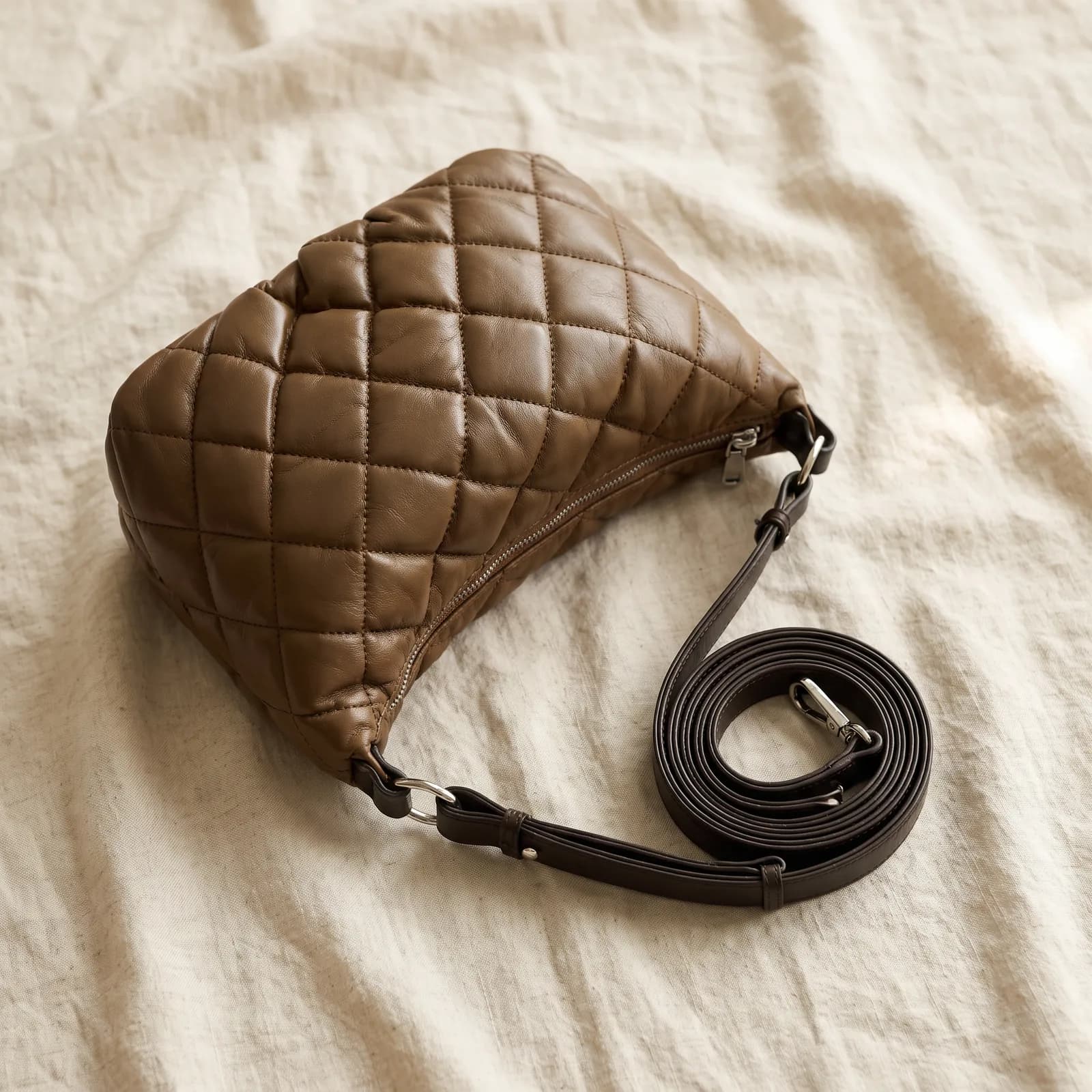 The crossbody bag laid top-down on warm cream linen with the strap coiled beside it