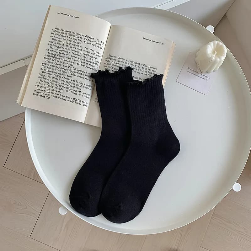 A pair of black ruffle ankle socks laid on a white table next to an open book