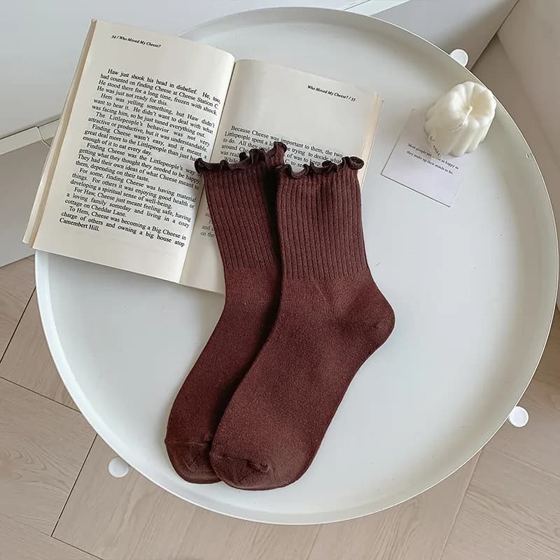 A pair of dark brown ruffle ankle socks resting on an open book on a white table