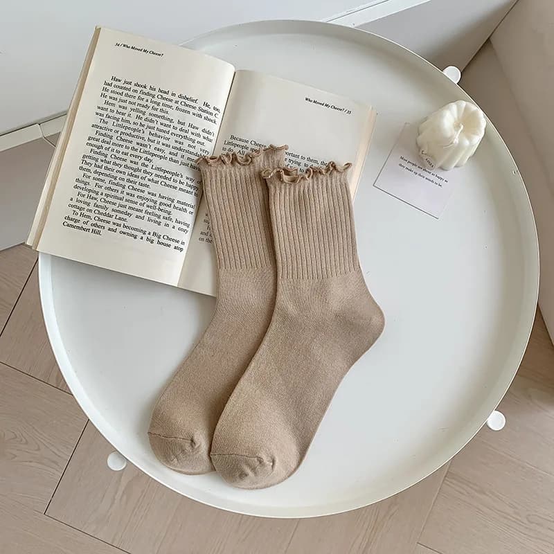 A pair of beige ruffle ankle socks resting on an open book on a white round table