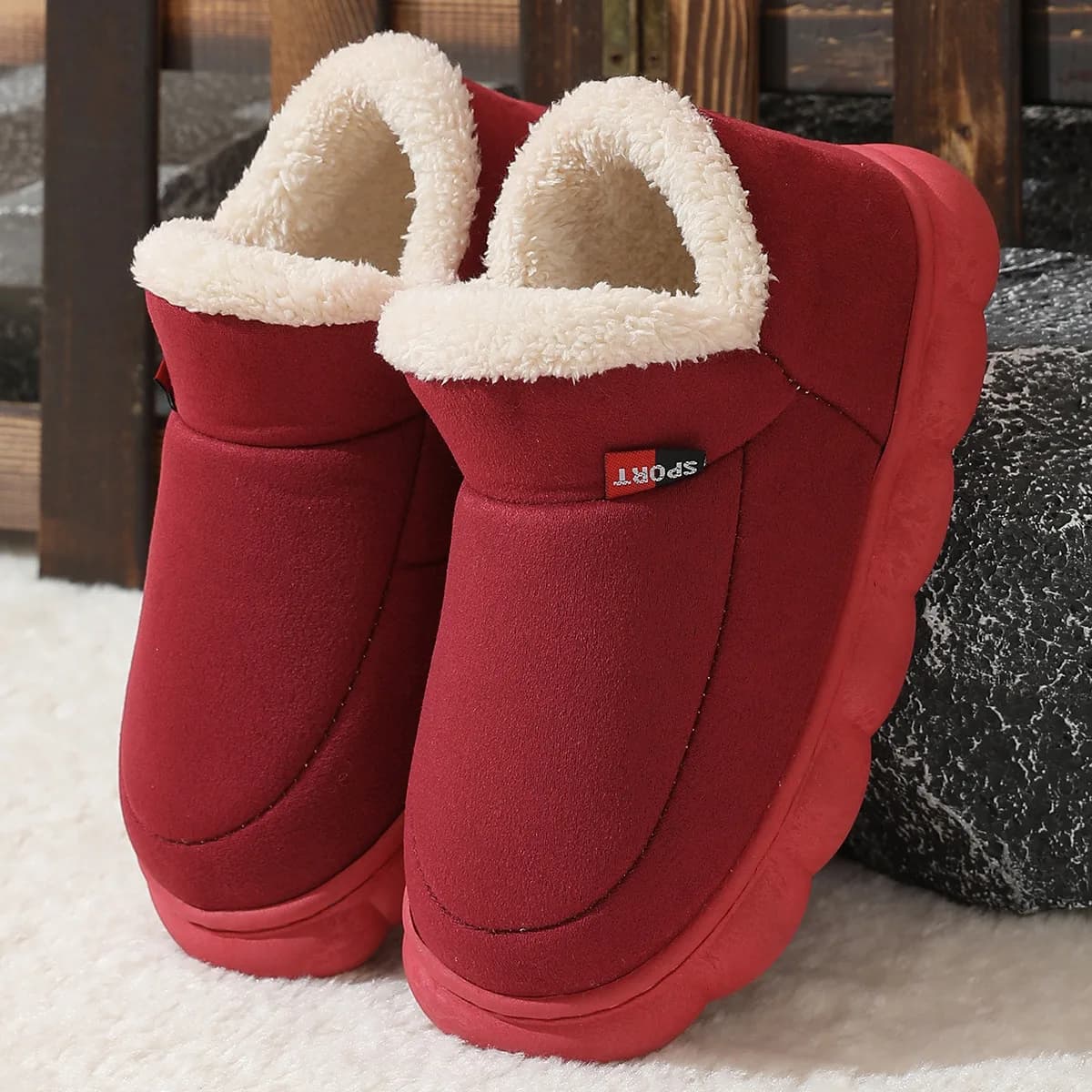 A pair of burgundy suede house shoes with white fleece lining resting on a textured surface