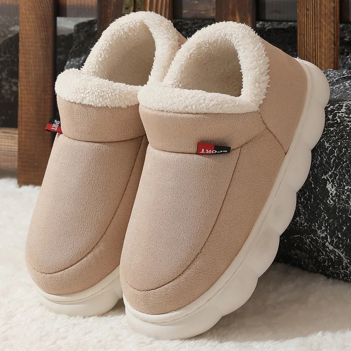 A pair of beige suede house shoes with white fleece lining and thick white soles