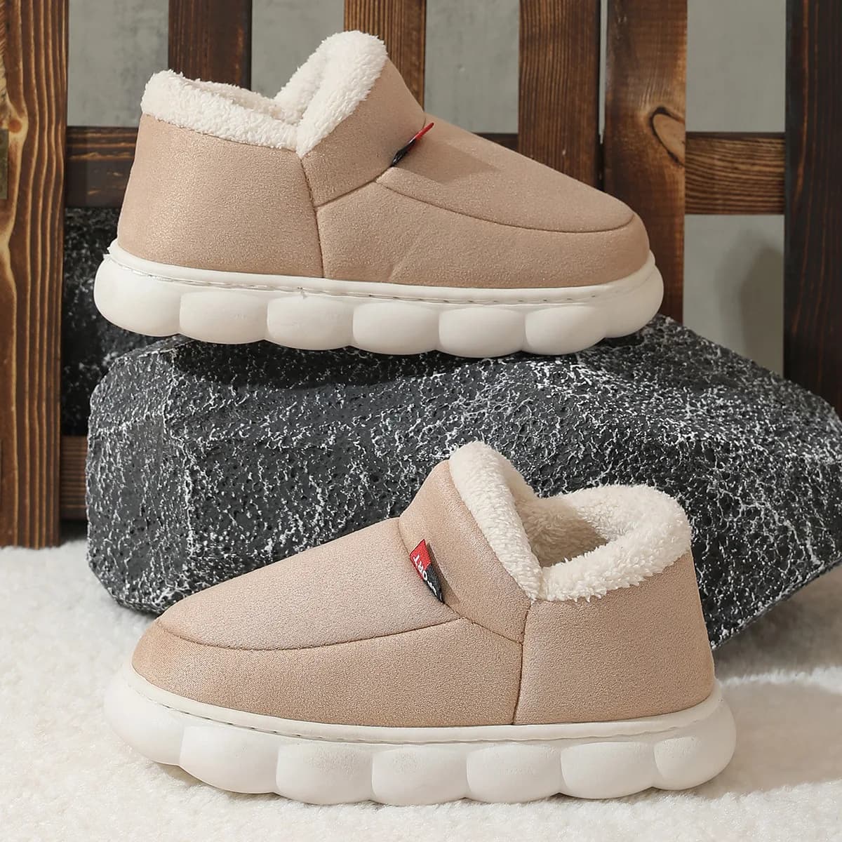 Two beige suede house shoes with white fleece lining stacked on a dark stone surface