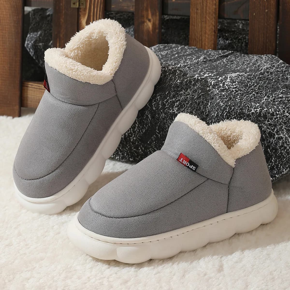 A pair of grey suede house shoes with white fleece lining resting on a textured surface