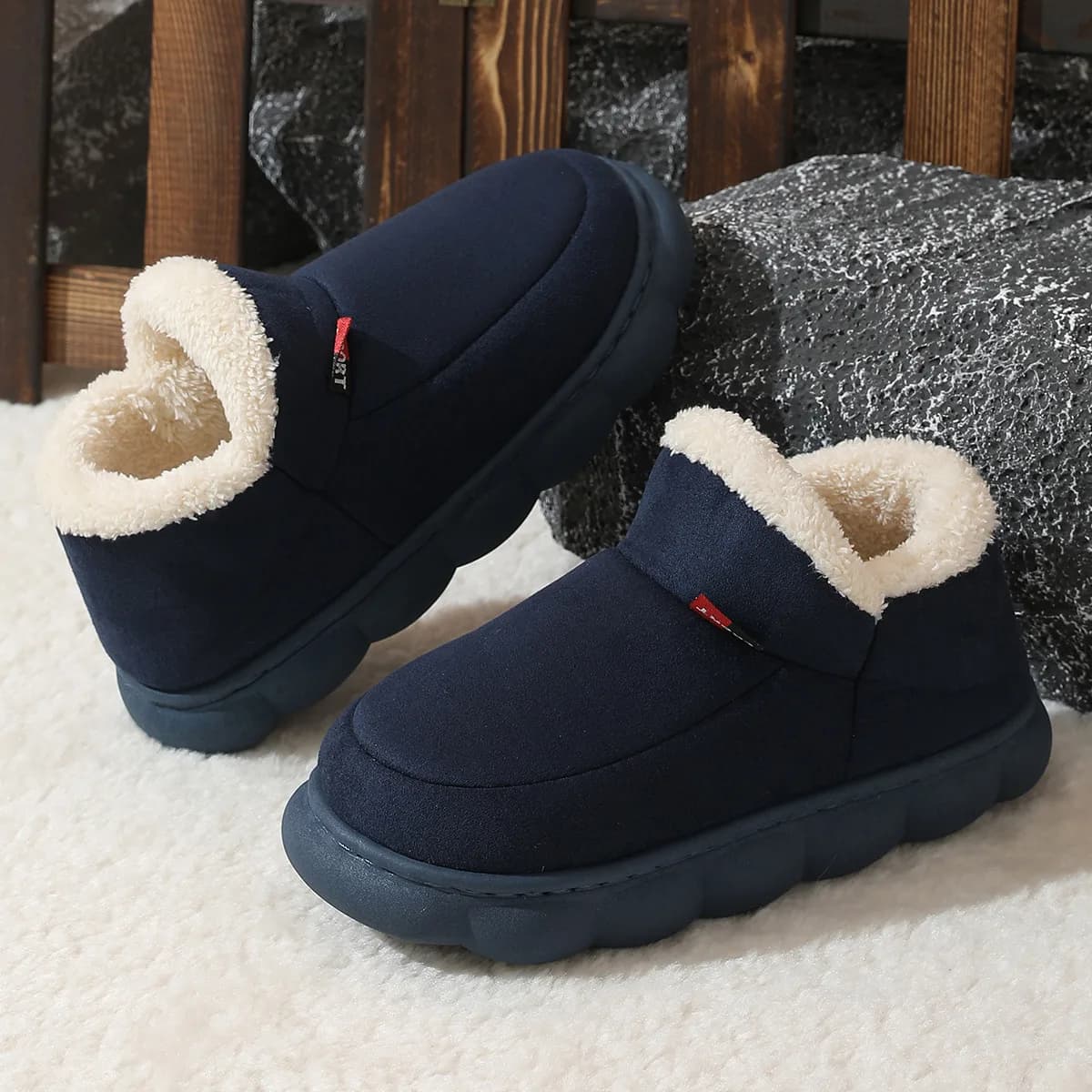 A pair of navy blue suede house shoes with cream-colored fleece lining resting on a textured surface