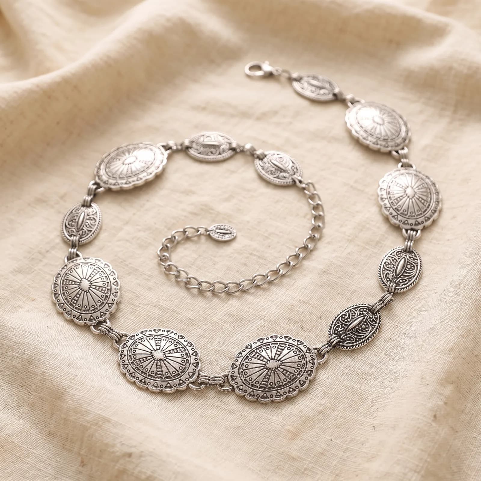 The concho belt laid top-down on warm cream linen in a loose curve