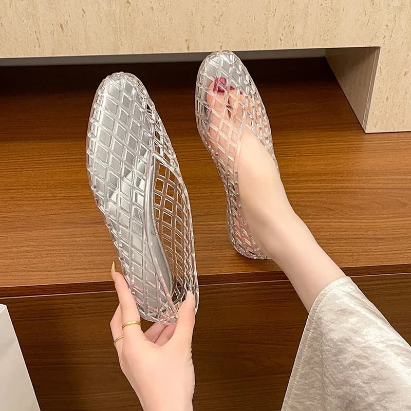 A person wearing clear woven jelly ballet flats with one shoe on their foot and the other held in their hand