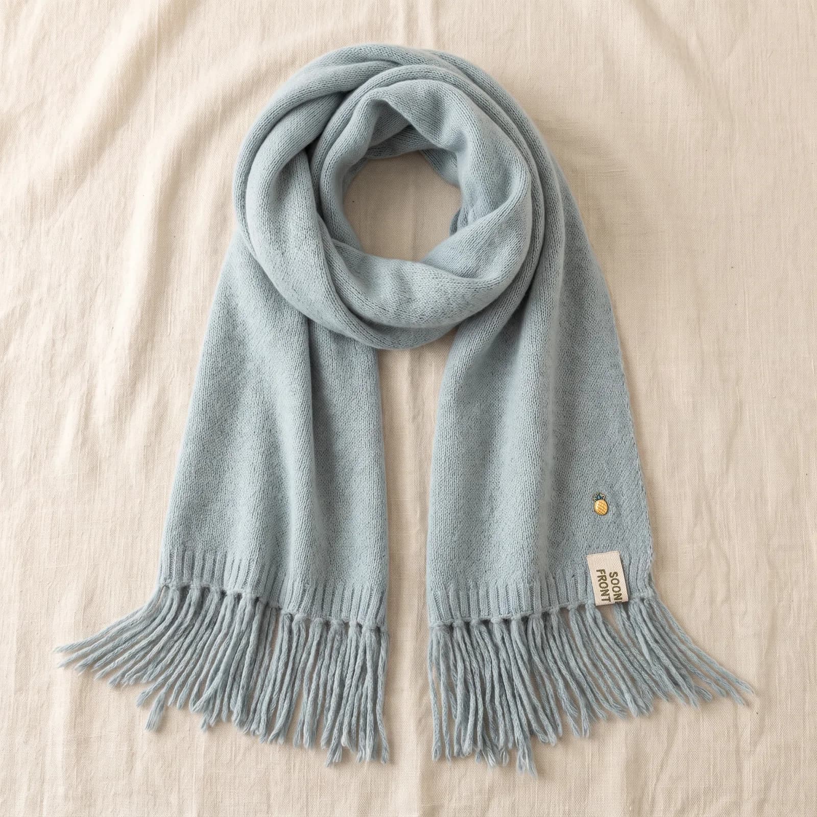 The scarf laid top-down on warm cream linen with the fringe fanned out