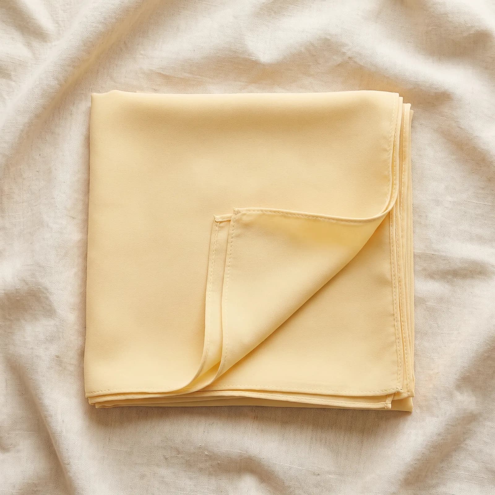 The shawl laid top-down on warm cream linen showing the solid pearl chiffon