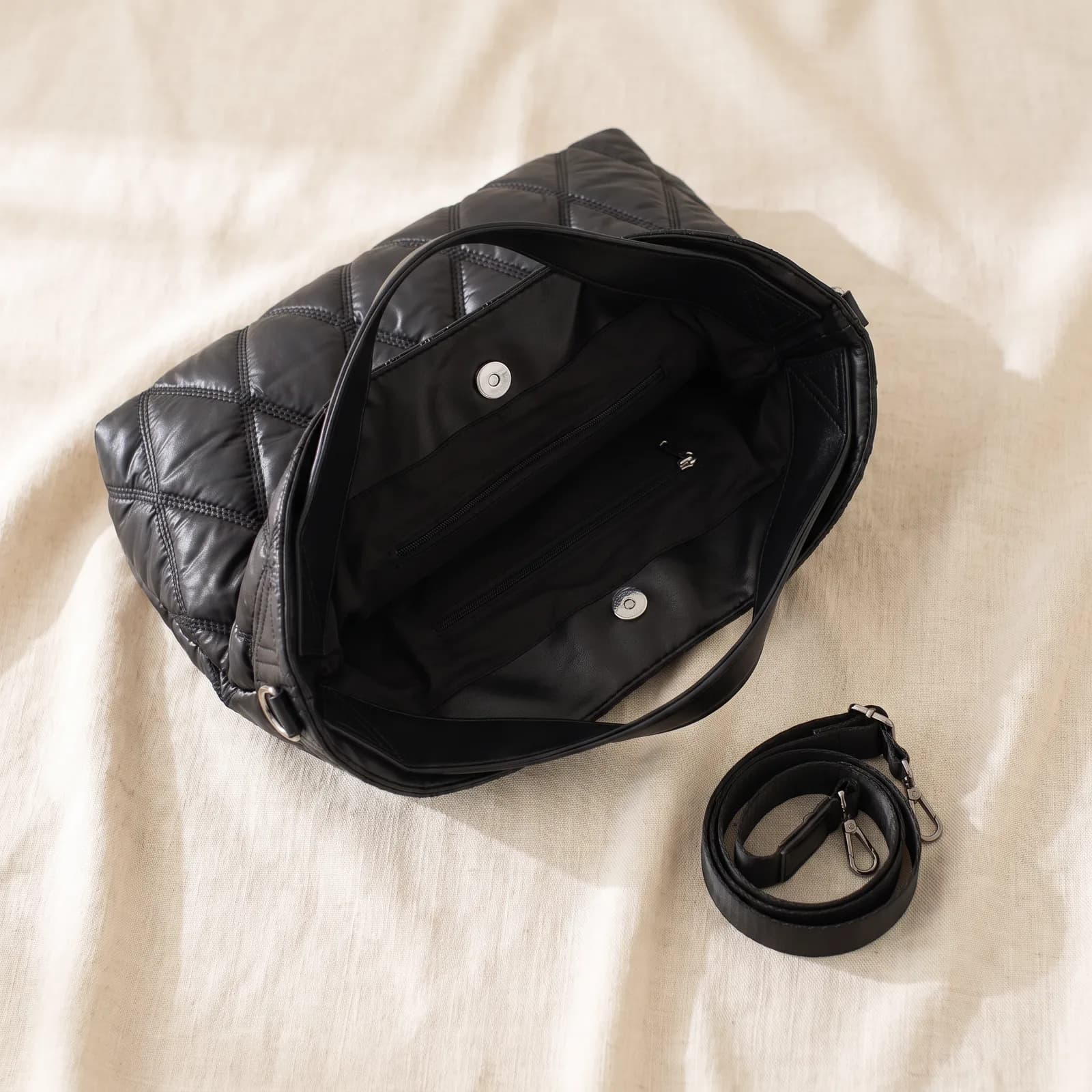 The tote laid top-down on warm cream linen with the shoulder strap coiled beside it