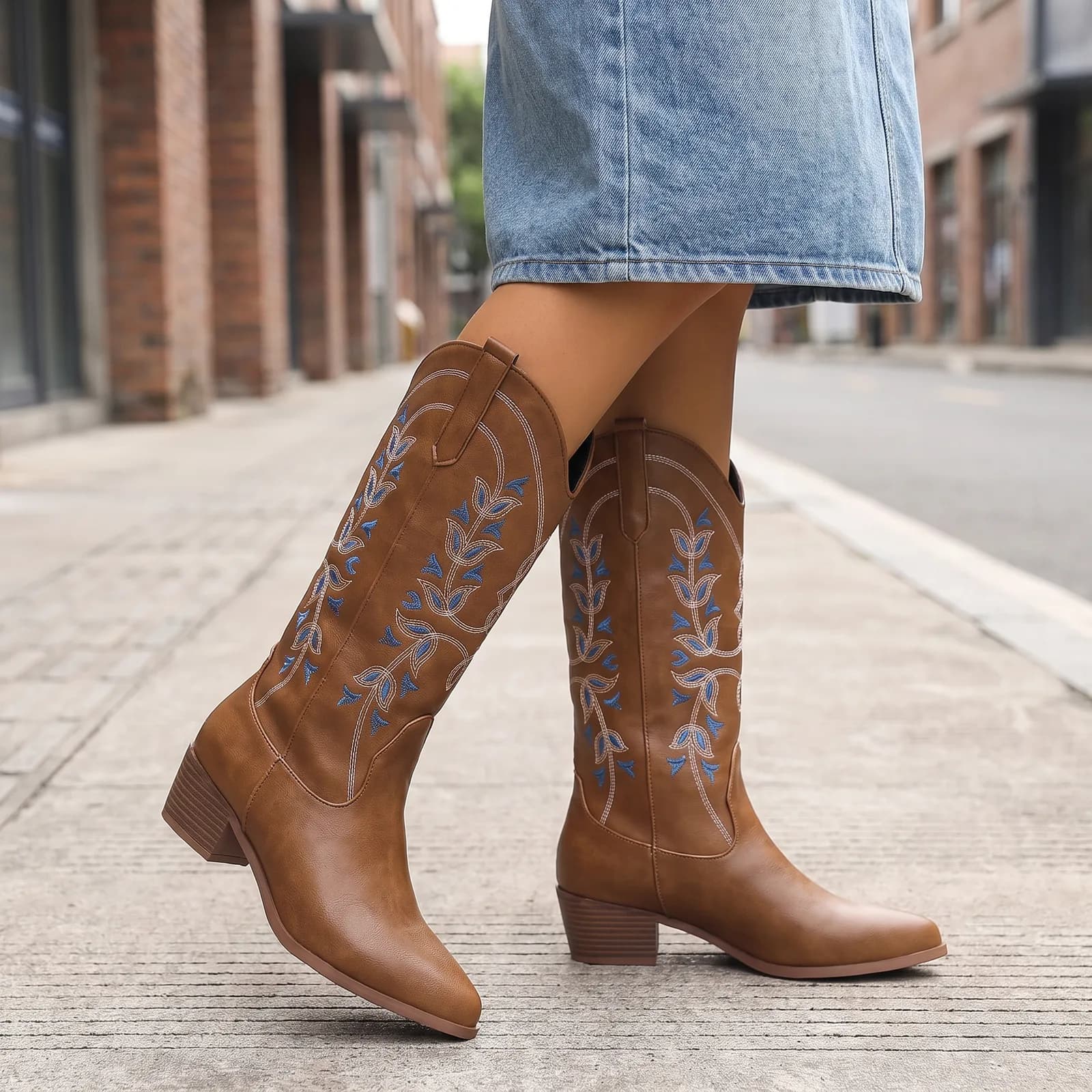 Legs from the knee down wearing the embroidered western boots with a denim skirt