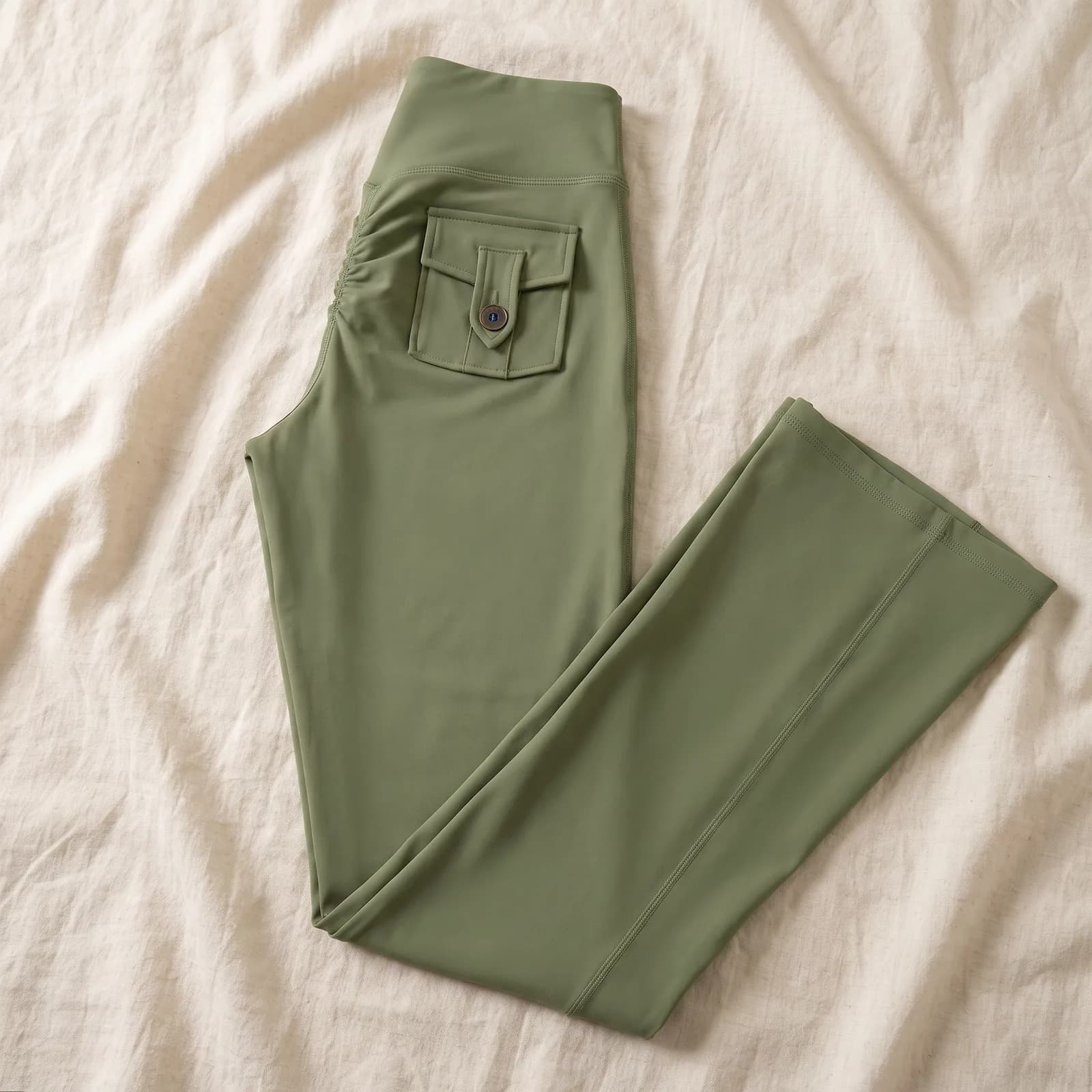 The leggings laid flat top-down on warm cream linen, back pocket visible