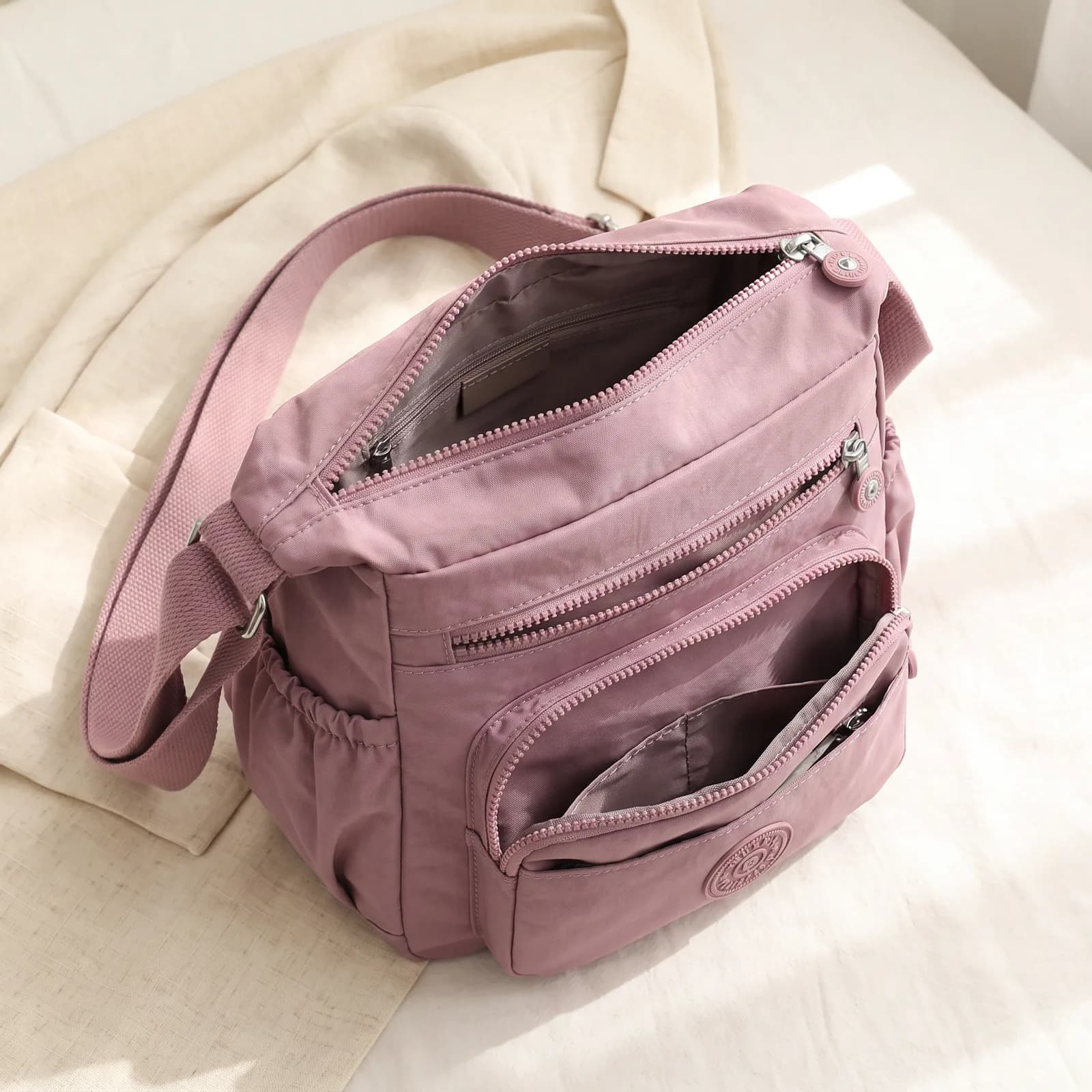 The crossbody bag laid top-down on warm cream linen showing all the front pockets