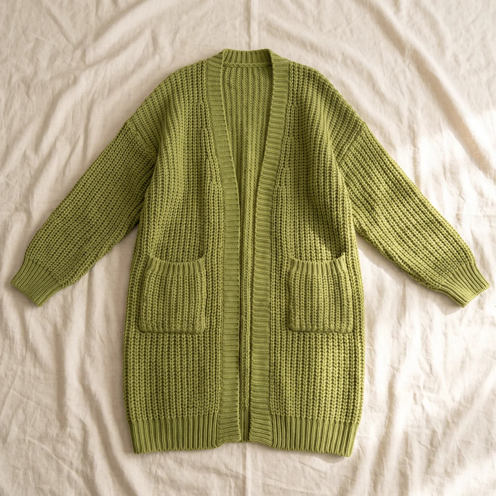 The cardigan laid flat top-down on warm cream linen, sleeves spread out