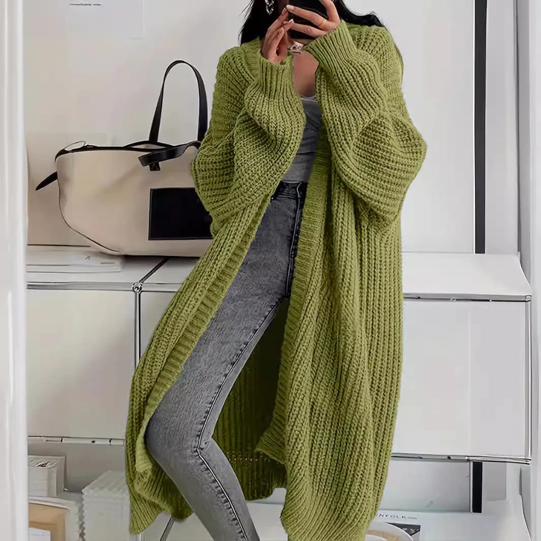 A woman wearing a longline olive green knit cardigan over a grey top and jeans