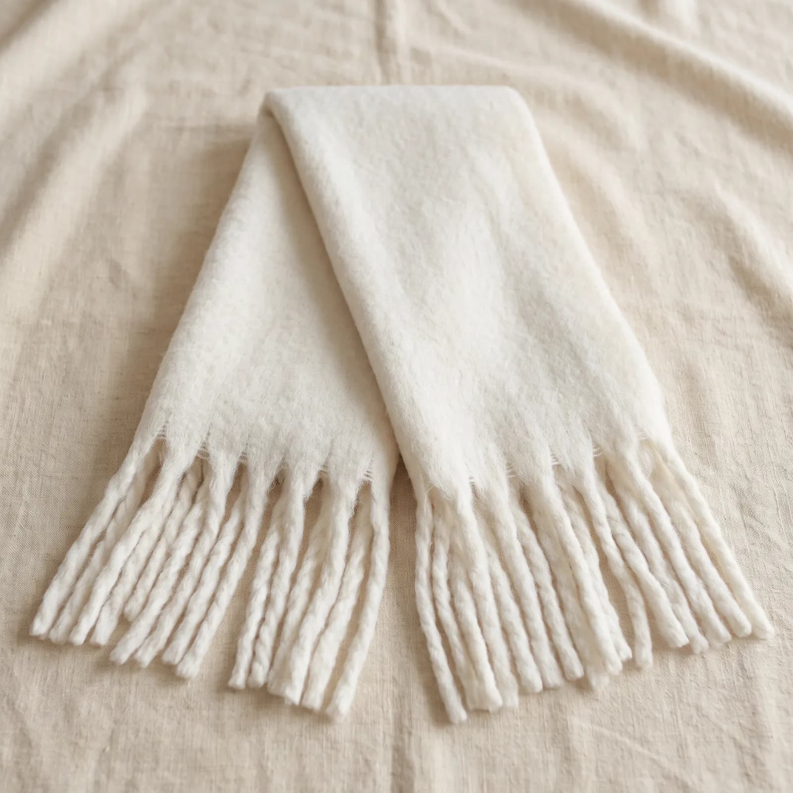 The scarf laid top-down on warm cream linen with the tassels fanned out