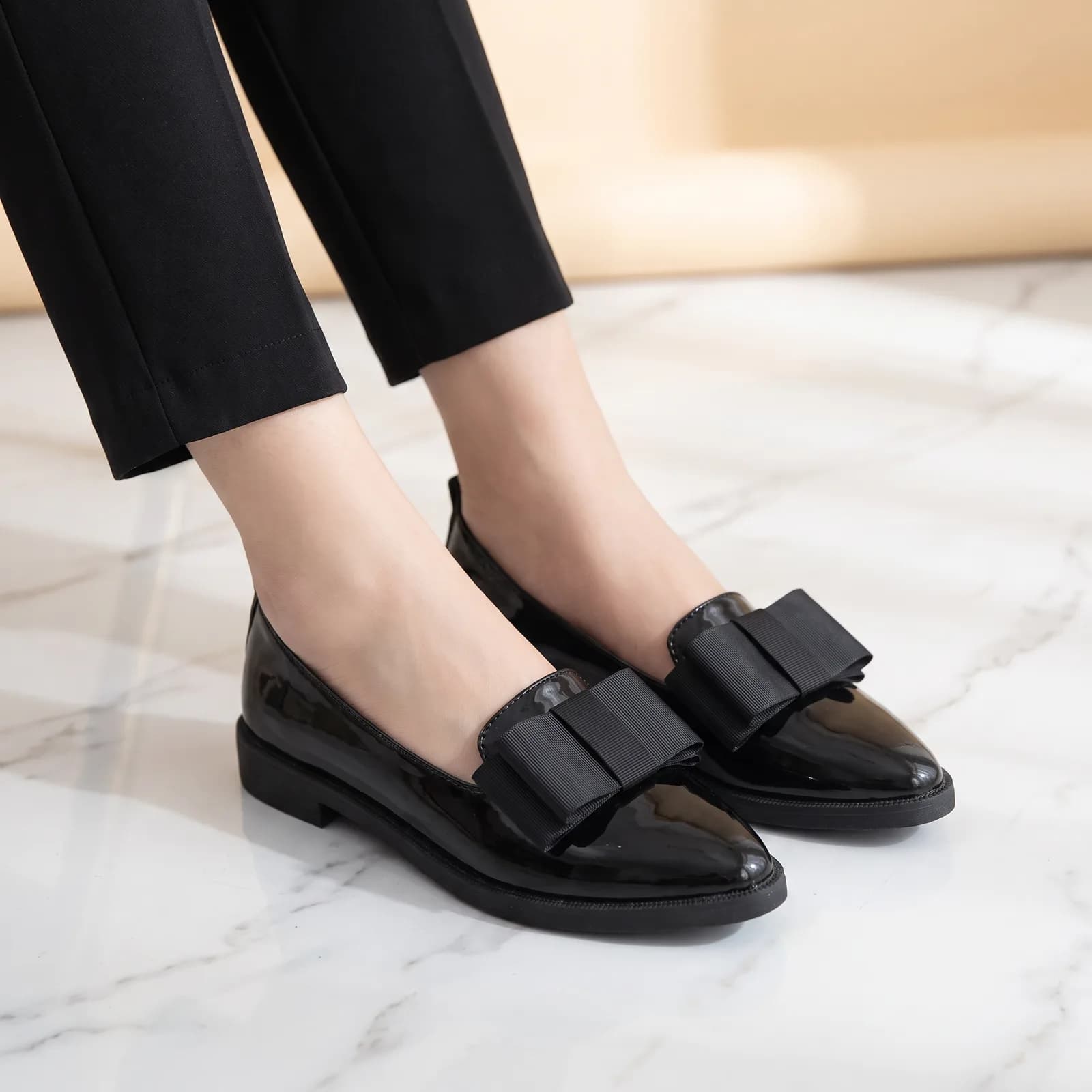 Feet from the ankle down wearing the patent bow flats with cropped trousers