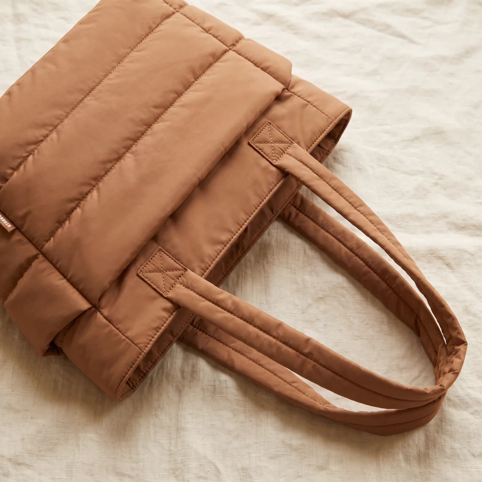 The tote laid top-down on warm cream linen, straps arranged beside it