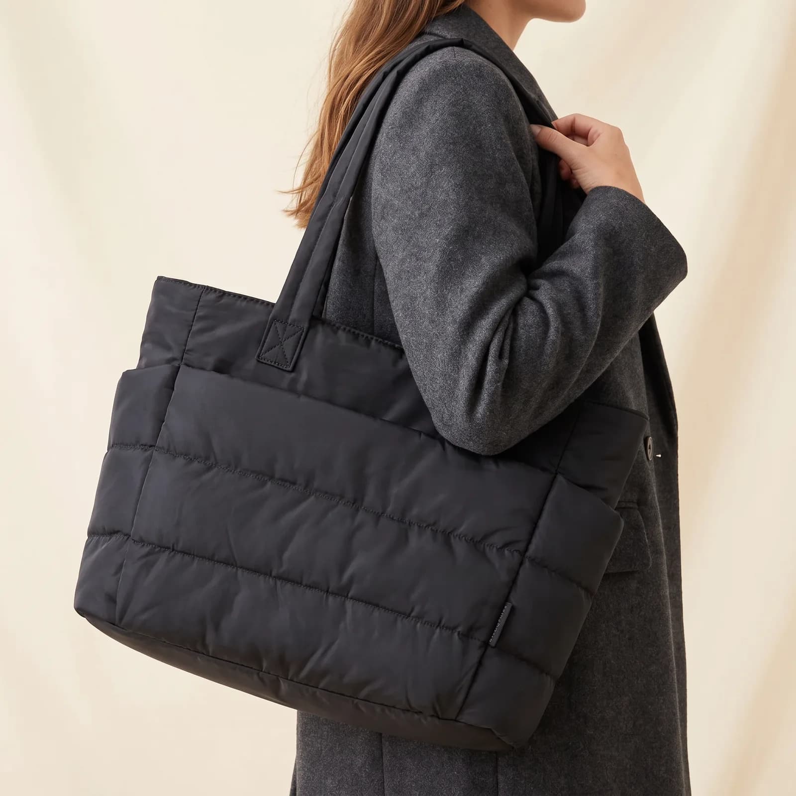 A tote bag worn on one shoulder over a coat, from the shoulder down, no face