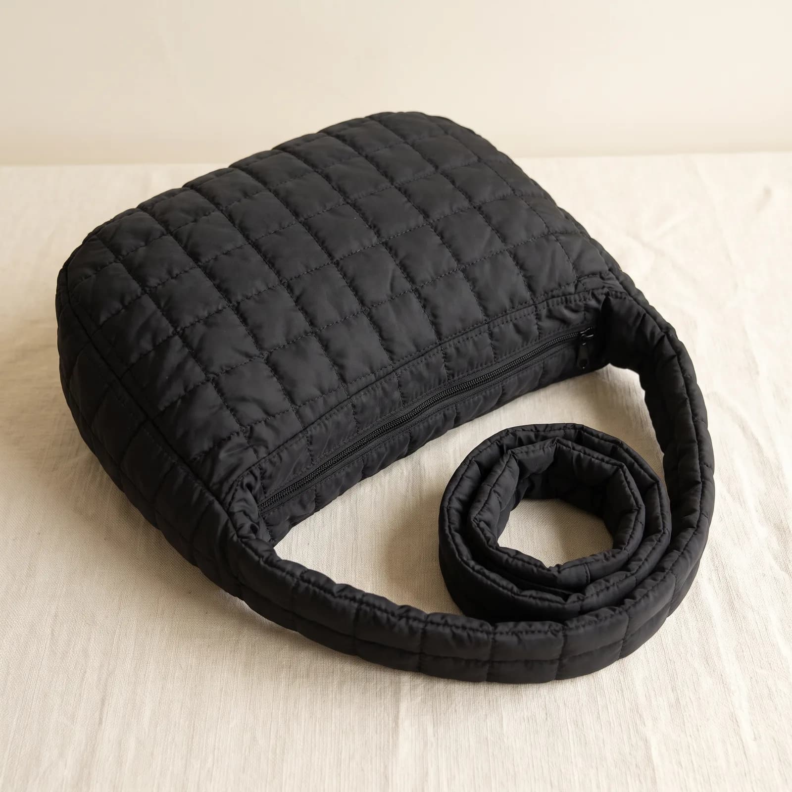The tote laid top-down on warm cream linen showing its quilted shape
