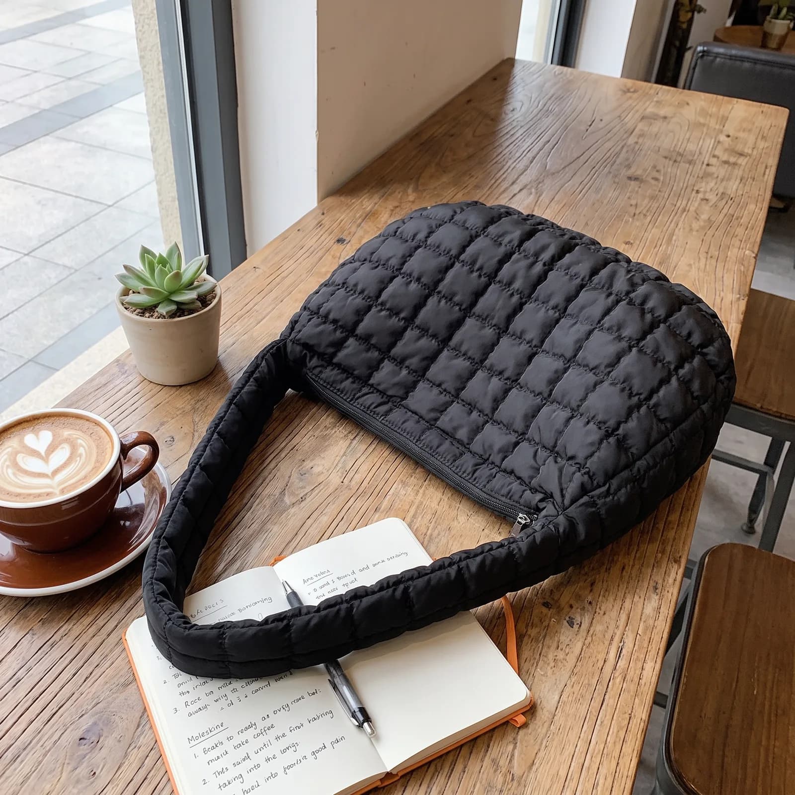 The tote set on a cafe chair next to a coffee cup and a notebook, no faces