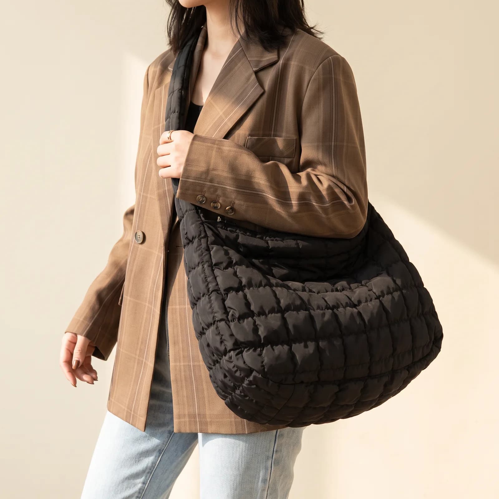A tote bag worn across the body over a blazer, from the shoulder down, no face