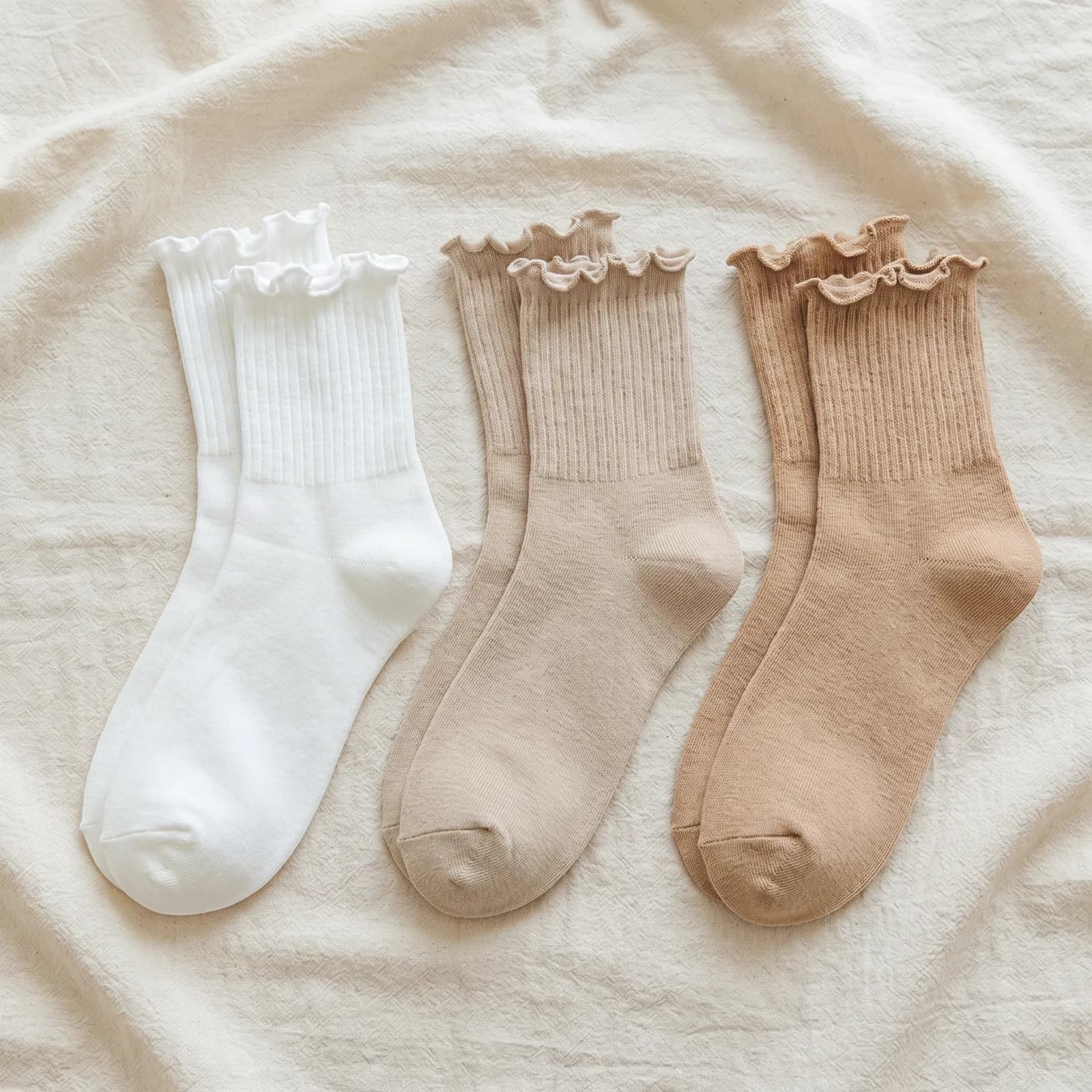 Three pairs of ruffle ankle socks laid top-down on warm cream linen