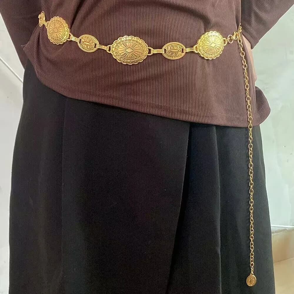 A gold western concho chain belt worn over a brown long-sleeve top and black skirt