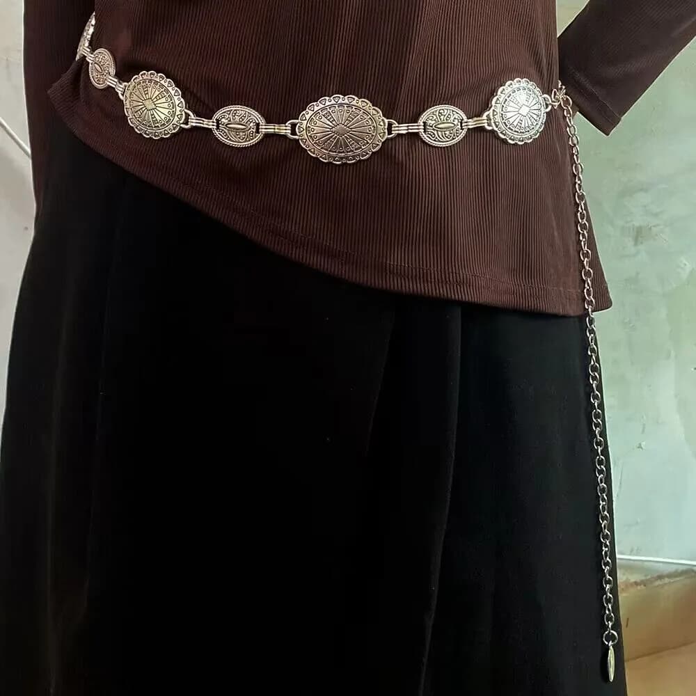 A silver Western concho chain belt worn over a brown ribbed top and black skirt