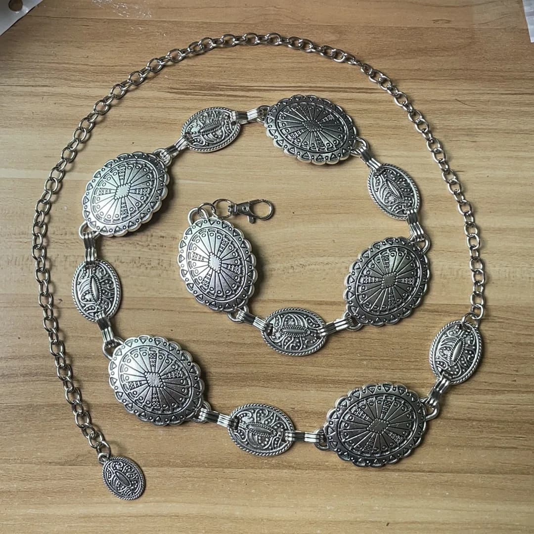 A silver western-style concho chain belt laid out on a wooden surface