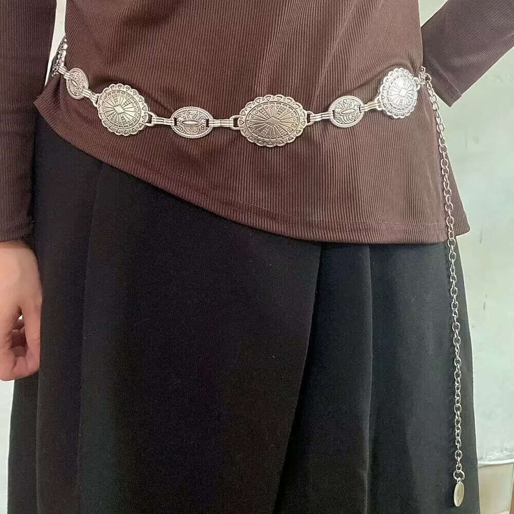 A silver western concho chain belt worn over a brown ribbed top and black skirt
